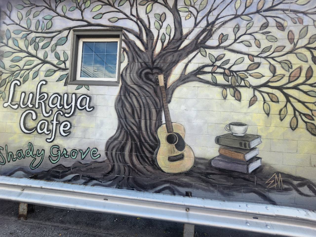 Detail of Lukaya Cafe's exterior mural showing the tree, guitar, books and cup